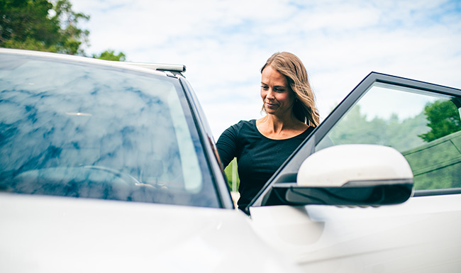 Kvinna med långt ljust hår och svart tröja kliver in i vit bil.